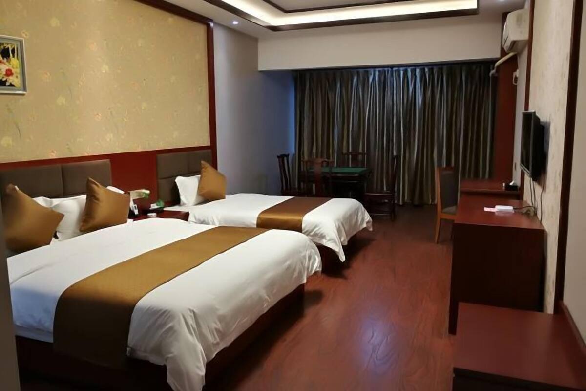 A hotel room with two beds, a desk, a chair, a television, and a curtain.