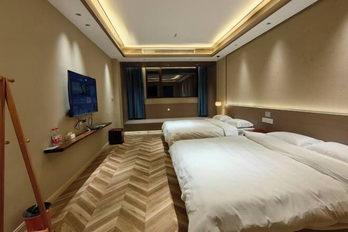 A hotel room with two beds, a herringbone-patterned carpet, a television on the wall, and a mirror above the bed.