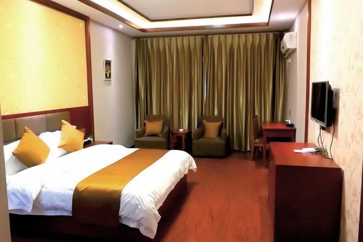 A hotel room with a bed, two armchairs, a desk, and a television.