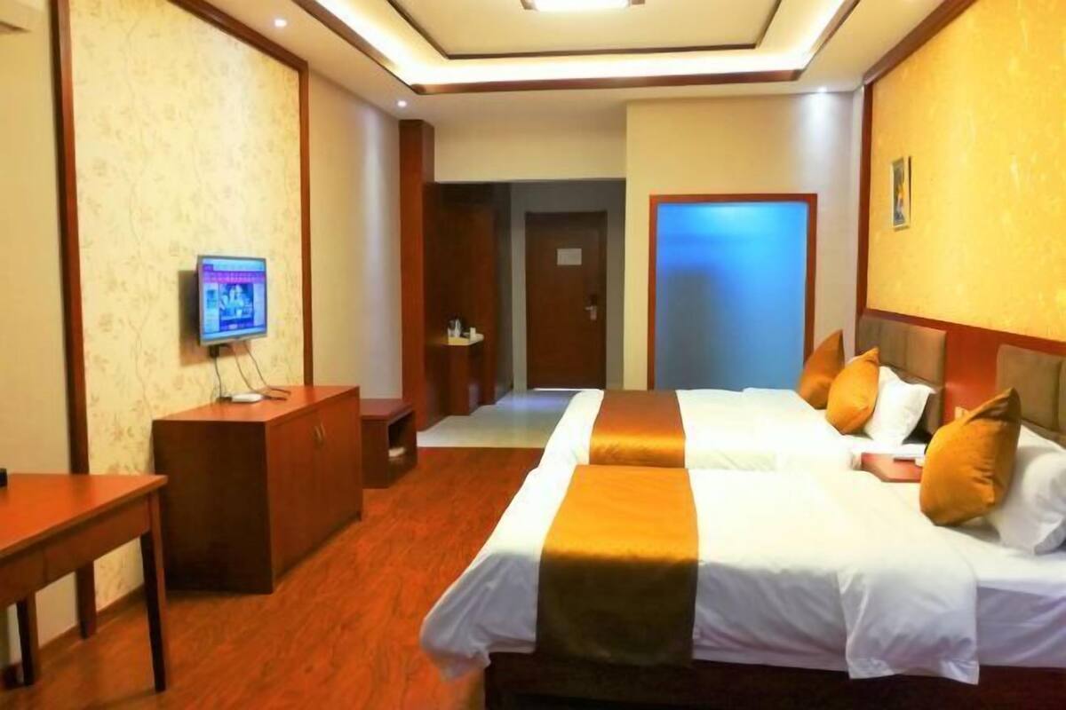 A hotel room with two beds, a desk, a television, and a mirror.