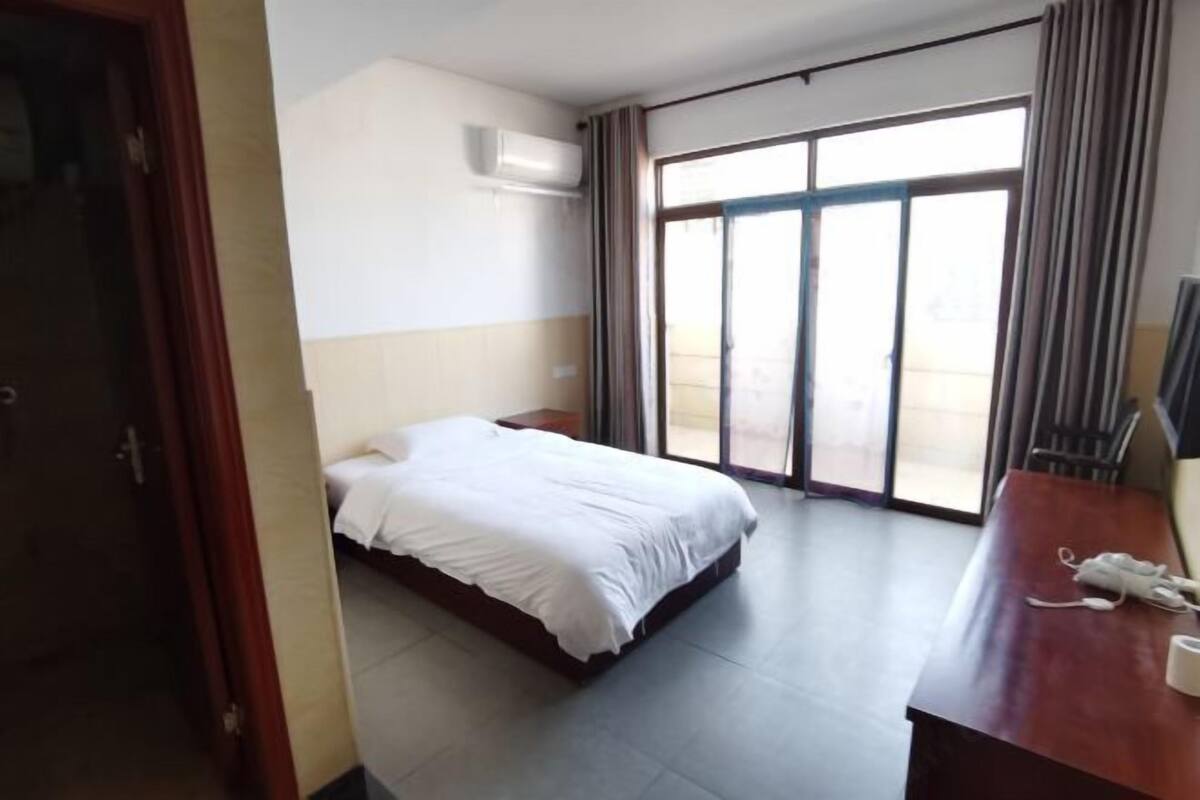 A hotel room with a bed, a desk with a telephone, and a sliding glass door leading to an outdoor area.