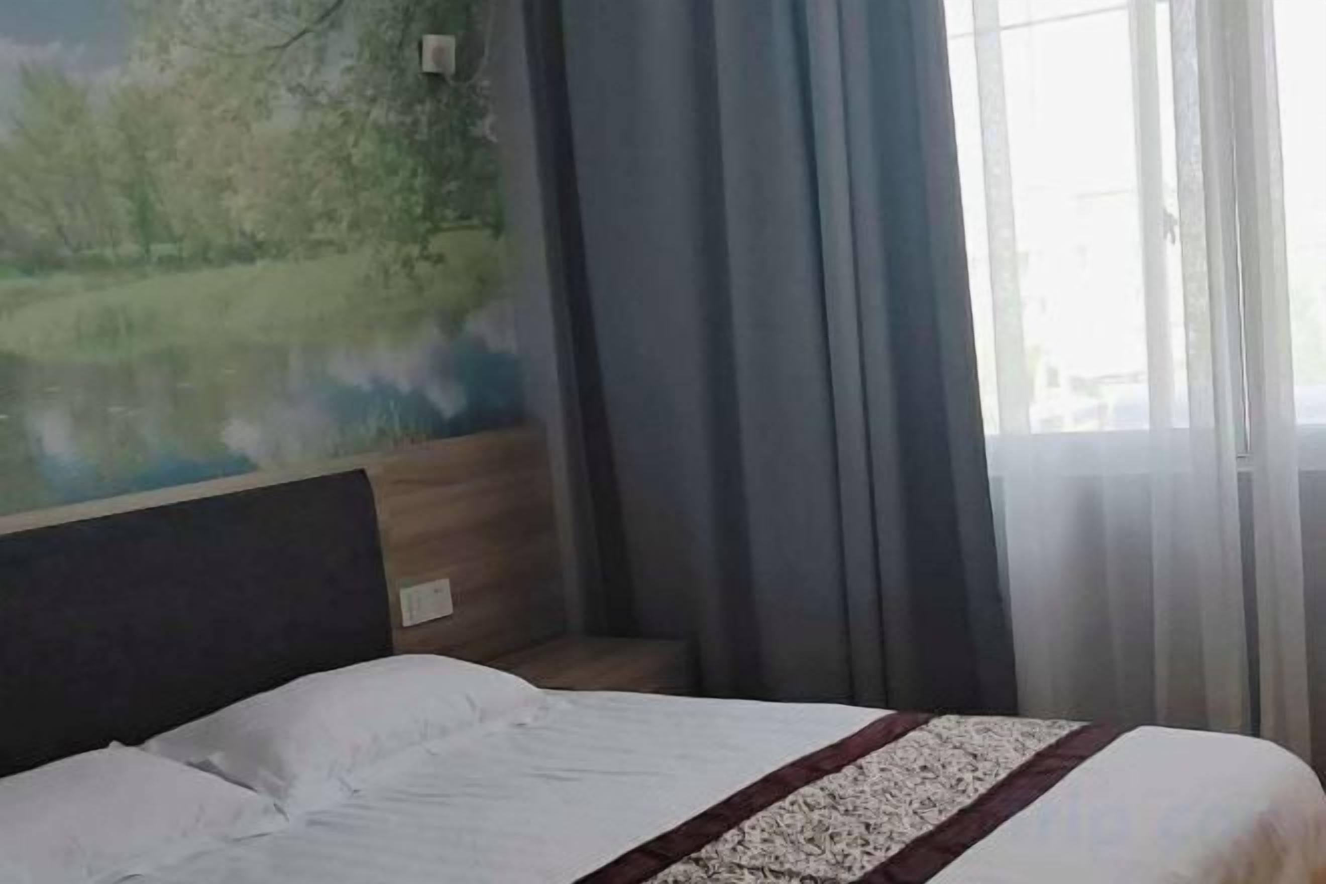 Habitación de hotel con cama, cabecero, ventana con cortinas y un mural en la pared.
