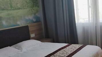 Habitación de hotel con cama, cabecero, ventana con cortinas y un mural en la pared.