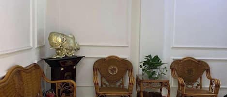 A room with four wicker chairs, a small table with a plant, and a decorative item on a stand.