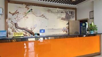 A reception desk with a traditional mural, a digital screen, and a plant.
