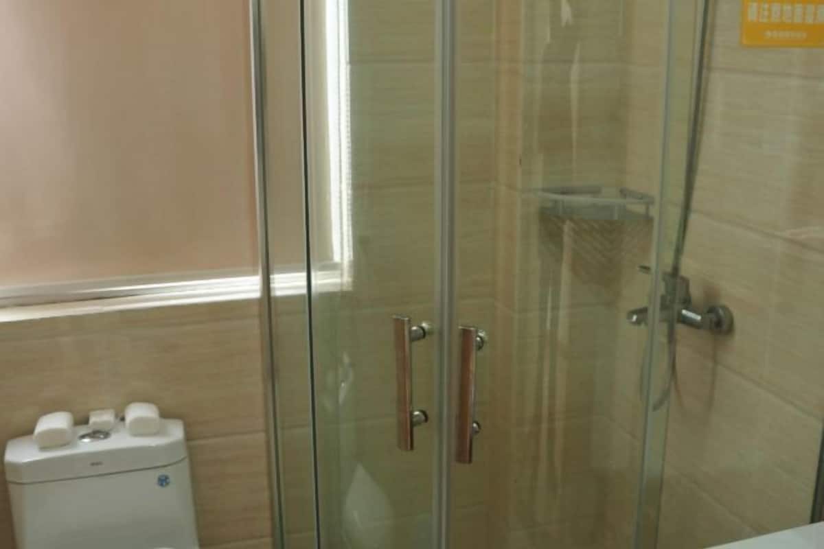 Un box de ducha con paredes de vidrio, un dispensador de toallas y un inodoro.