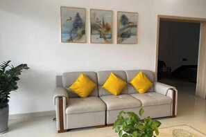 A living room with a sofa, three paintings on the wall, and two potted plants. - Guli Business Hotel (Yuyao)