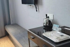 A hotel room with a bed, a desk with a kettle, a television, and a power outlet. - Guli Business Hotel (Yuyao)