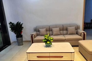 Una sala de estar con un sofá color beige, una mesa de centro con un florero y una planta en maceta.