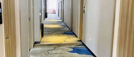 A hotel corridor with doors on both sides, a patterned carpet, and a light-colored wall.