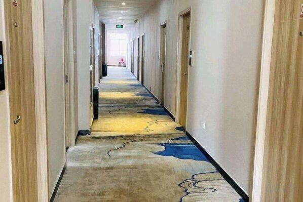 A hotel corridor with doors on both sides, a patterned carpet, and a light-colored wall. - Guli Business Hotel (Yuyao)