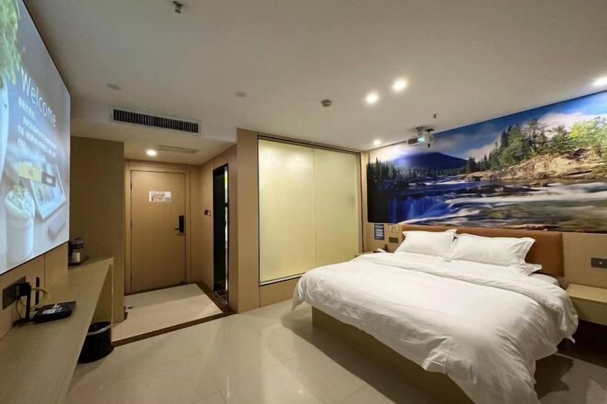 A hotel room with a bed, a TV screen, a wardrobe, and a mural of a river scene.