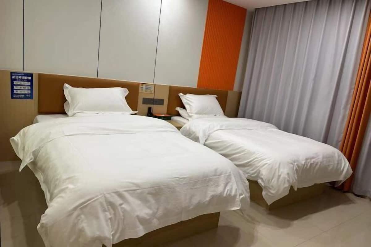 A hotel room with two single beds, a wooden headboard, a nightstand, and a curtain.