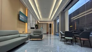 A modern lobby with a sofa, armchairs, and a dining area with chairs. - Ganzhou Yuekelong Holiday Hotel (Ganzhou)