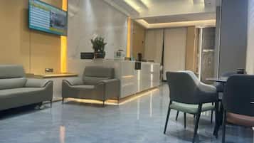 A hotel lobby with a reception desk, seating area, and a large screen.