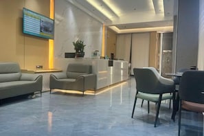 Un vestíbulo de hotel con una recepción, zona de estar y una pantalla grande.