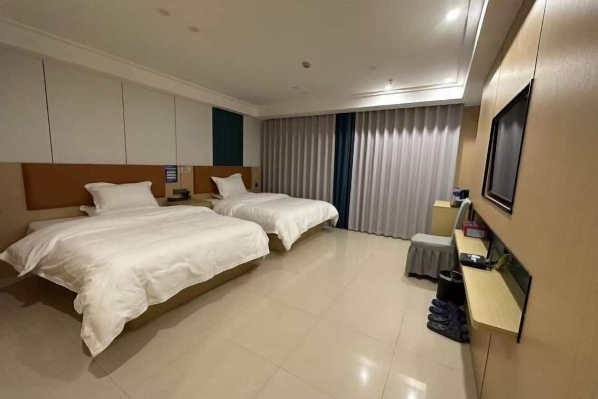 A hotel room with two beds, a small desk, a TV, and a window with curtains.