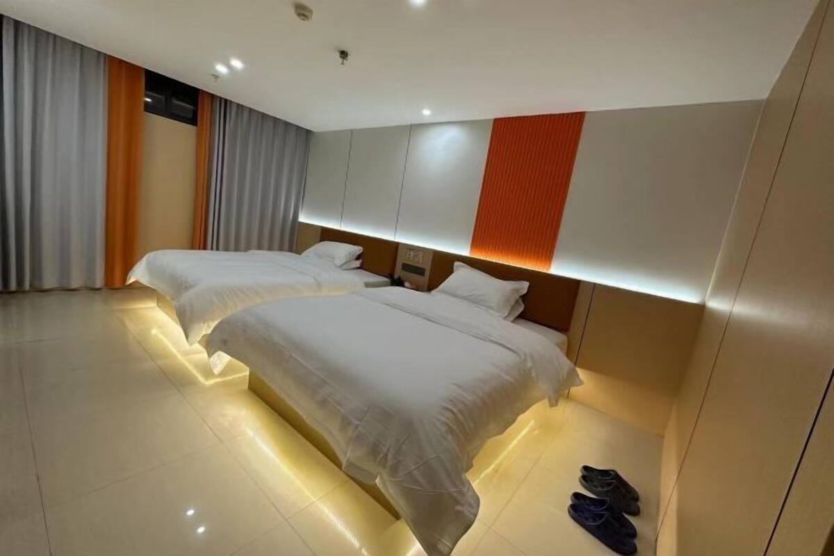 A hotel room with two beds, a large window with curtains, and a pair of shoes on the floor.