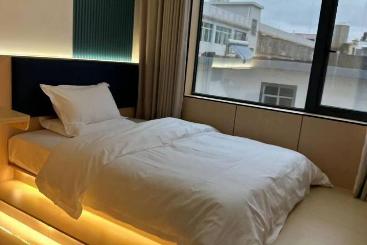 A hotel room with a bed, a nightstand, and a window with a view of buildings.