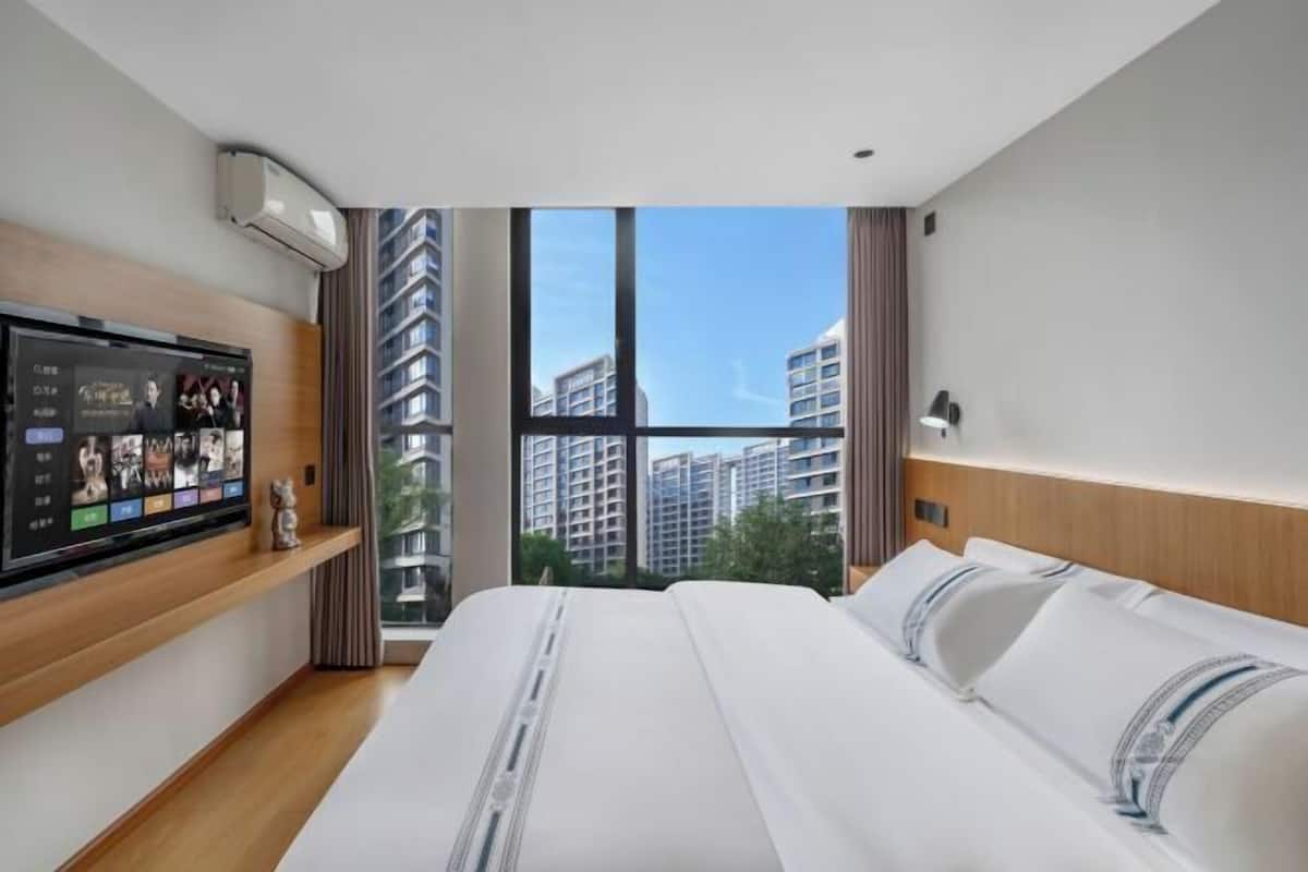 Quarto de hotel com uma cama grande, uma TV em uma estante de madeira e vista para edifícios altos.