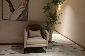 En stol i en hall med ett mönstrat mattgolv, en krukväxt och en väggmonterad lampa.