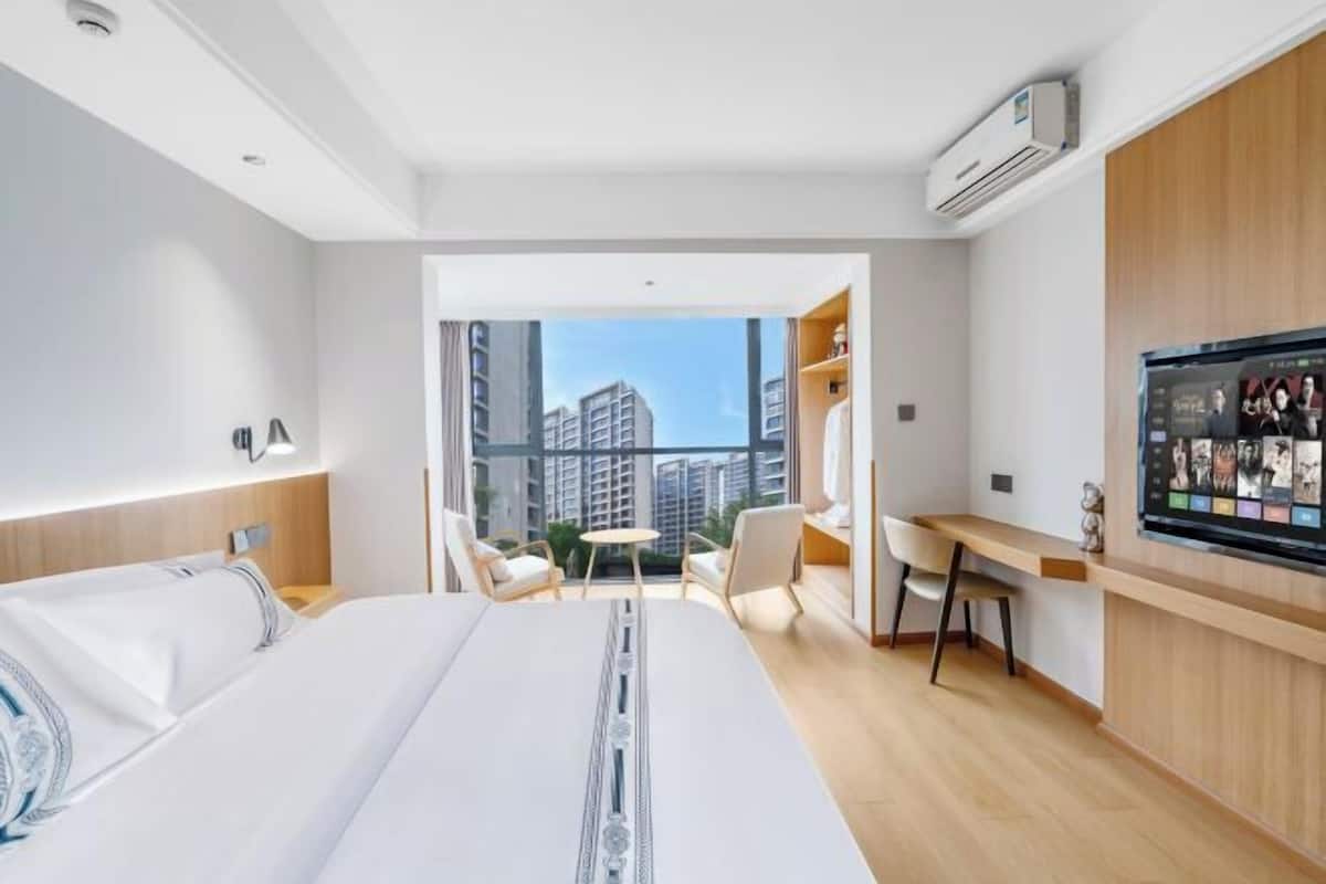 Quarto de hotel com cama, escrivaninha, cadeira, televisão e vista para edifícios altos.