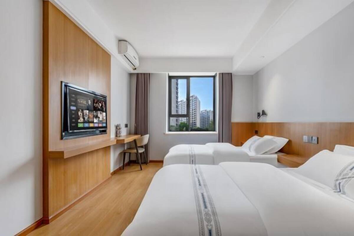 Quarto de hotel com duas camas, uma escrivaninha e uma janela grande com vista para a cidade.