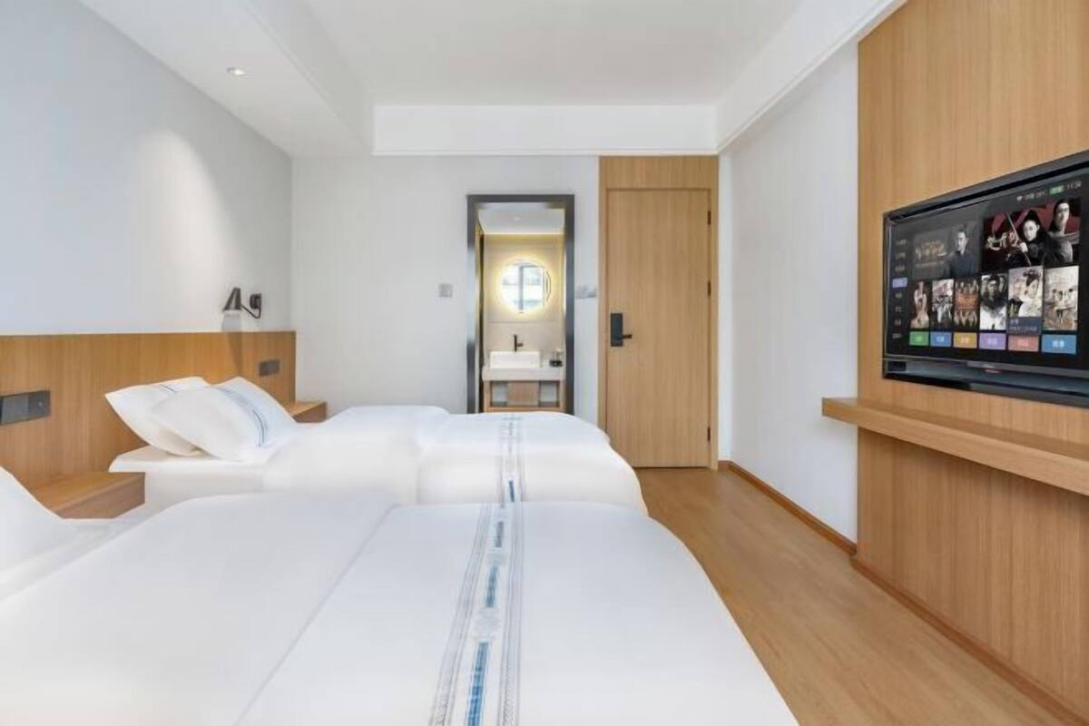 Quarto de hotel moderno com uma cama grande, uma televisão na parede e uma porta de madeira para o banheiro.