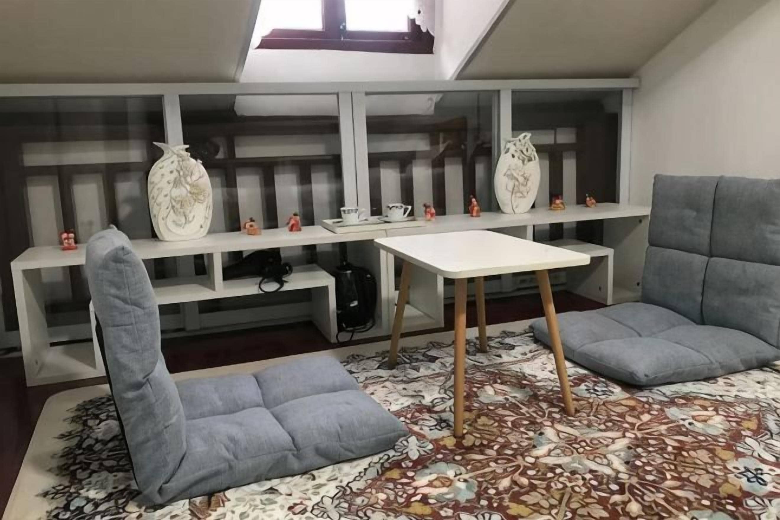 A room with a loft bed, a small table, two grey sofas, and a patterned rug.