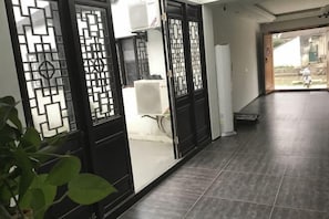 Un couloir avec des portes décoratives noires, un sol carrelé et une vue sur l’extérieur.