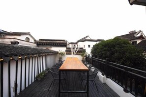 A traditional wooden deck with a long table and chairs, surrounded by white buildings with black railings. - Muxiju Guesthouse (Suzhou)