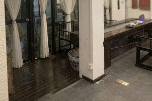 Una habitación con piso de madera oscura, un pilar blanco, una mesita con un tazón azul y una silla.