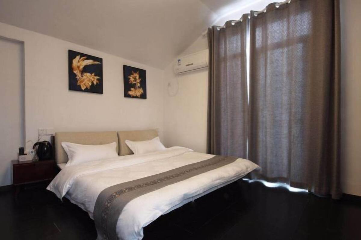 Een hotelkamer met een groot bed, twee wanddecoraties, een donkere vloer en een raam met gordijnen.