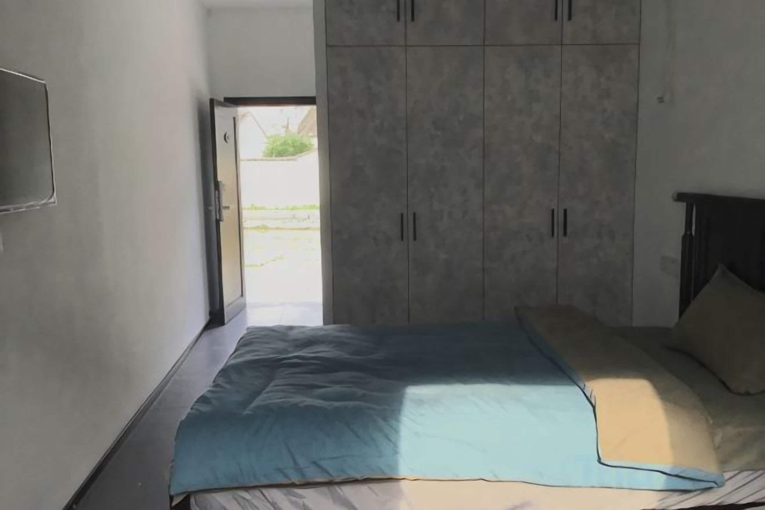 A bedroom with a bed, a wardrobe, and a door leading to an outdoor area.