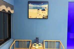 A room with a blue wall, a framed painting of a beach scene, and two wooden chairs with a small table between them. - Muxiju Guesthouse (Suzhou)