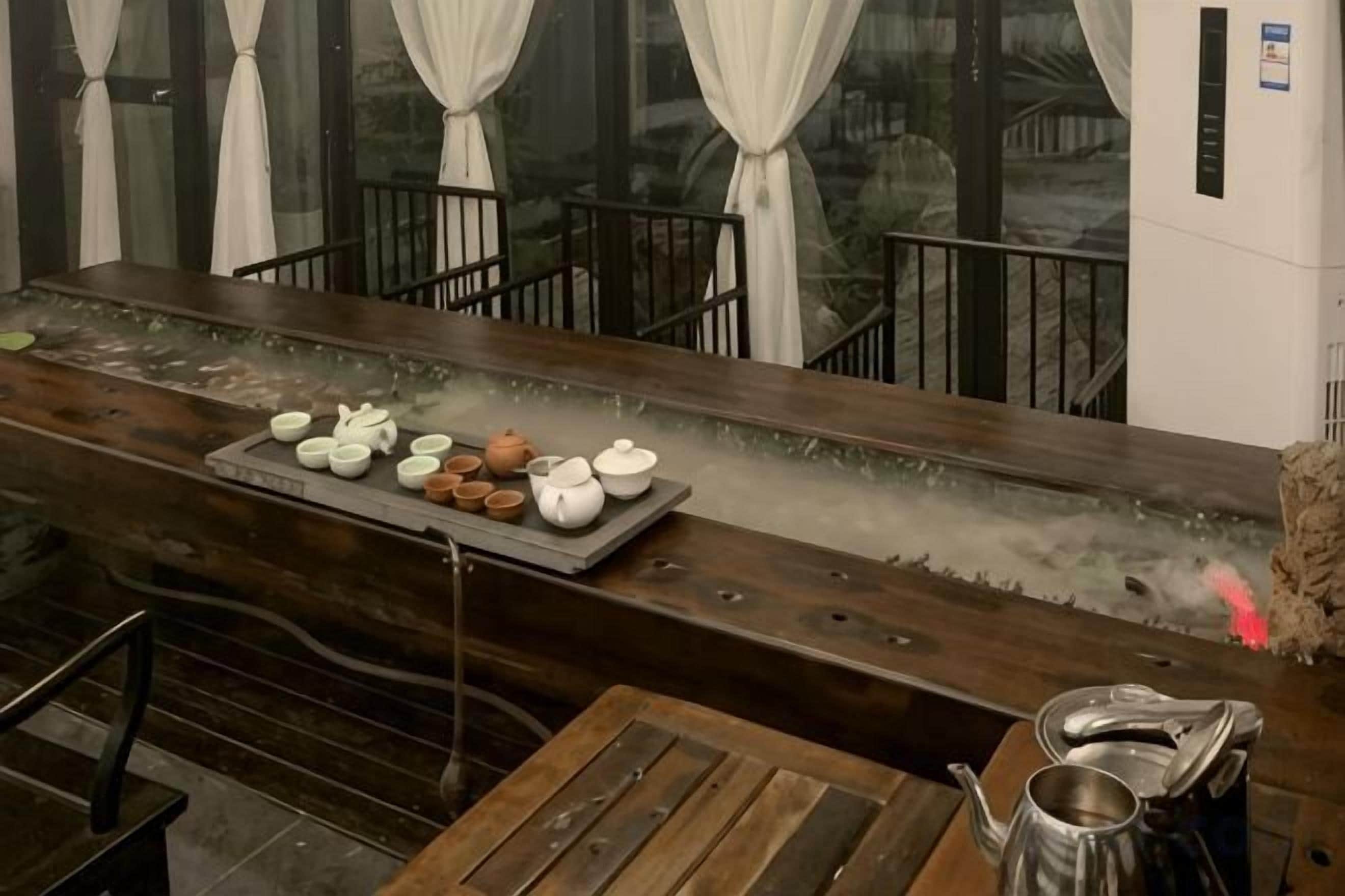A wooden bar area with a long counter, a tray of teapots, and a seating area with a table and chairs.