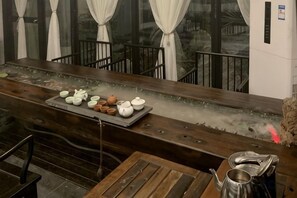 Zona de bar con barra de madera, una bandeja de teteras y un espacio de estar con mesa y sillas.
