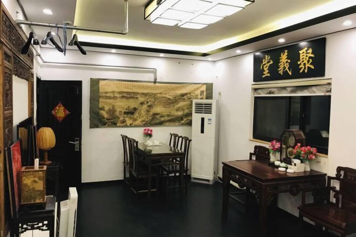 Een traditionele Chinese kamer met een eettafel, stoelen en een groot wandkleed.