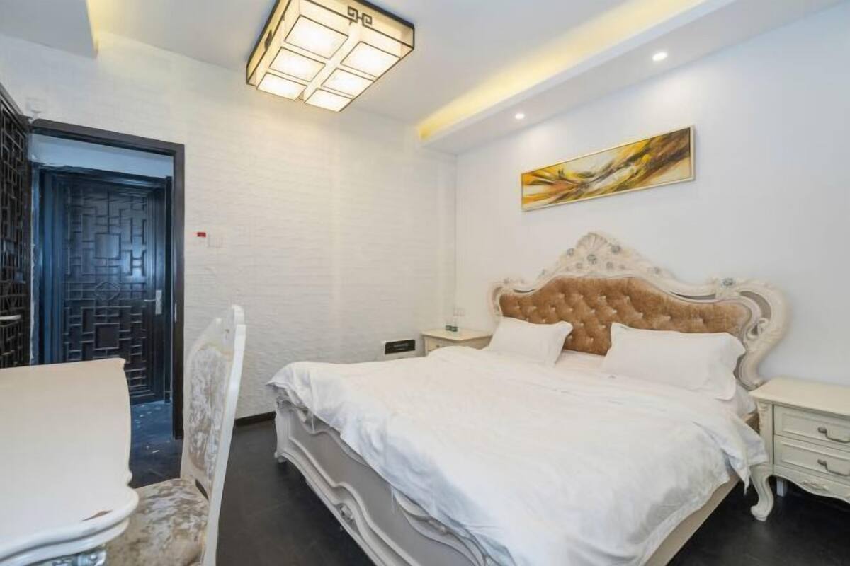 Een slaapkamer met een groot bed, een nachtkastje, een stoel en een deur met een geometrisch patroon.