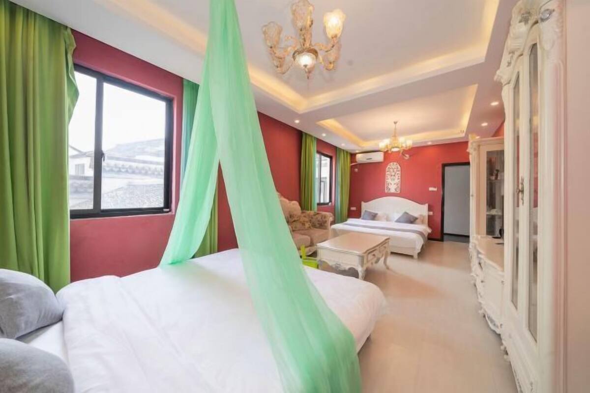 Een hotelkamer met twee bedden, een kroonluchter, een groot raam met gordijnen en uitzicht op buiten.