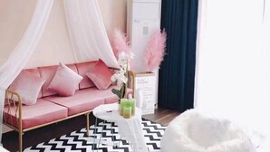 Ein Zimmer mit einem rosafarbenen Sofa, einem weißen Stuhl, einem kleinen runden Tisch mit Kerzen und einem weißen, flauschigen Sessel.