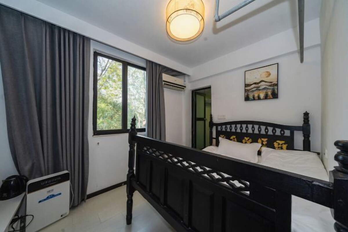 A bedroom with a bed, a window with curtains, an air conditioning unit, and a painting on the wall.