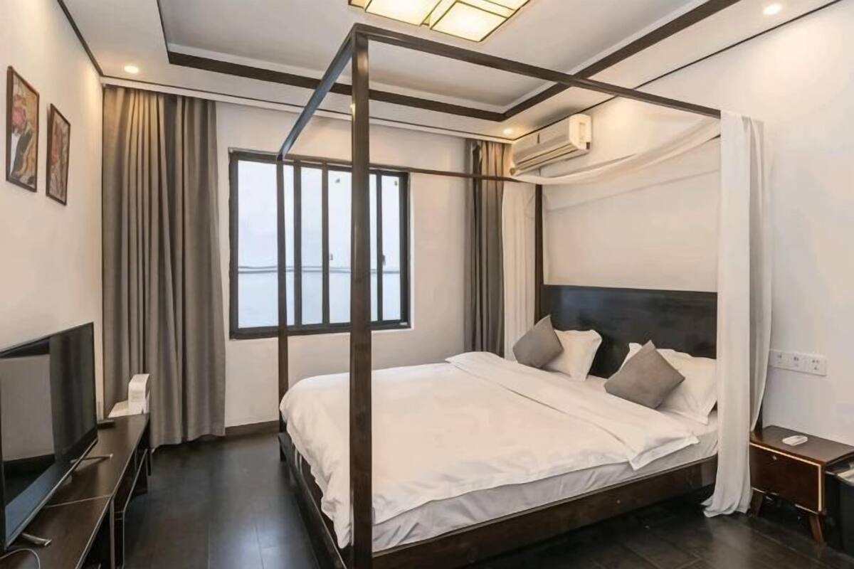 Een hemelbed met een donker hoofdbord, een flatscreen televisie en een nachtkastje.