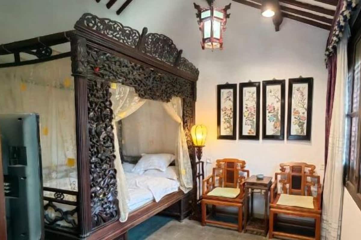 A traditional room with a four-poster bed, a table with chairs, and framed artwork on the wall.