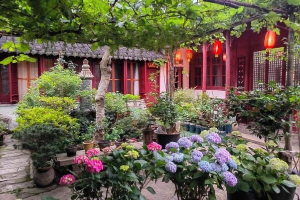 A traditional courtyard with potted plants and a red building with tiled roof.