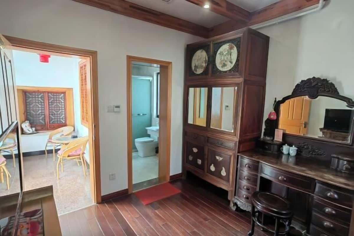 A room with a wooden floor, a cabinet with drawers, a stool, and a door leading to another room.