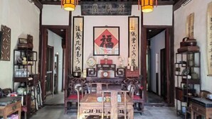 Un intérieur traditionnel avec une table et des chaises en bois au centre, entourées d’étagères remplies de divers objets.