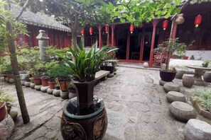 A courtyard with stone flooring, potted plants, and traditional red architecture.