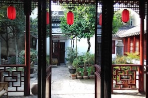 Una entrada con una puerta tradicional, plantas en macetas y faroles rojos.
