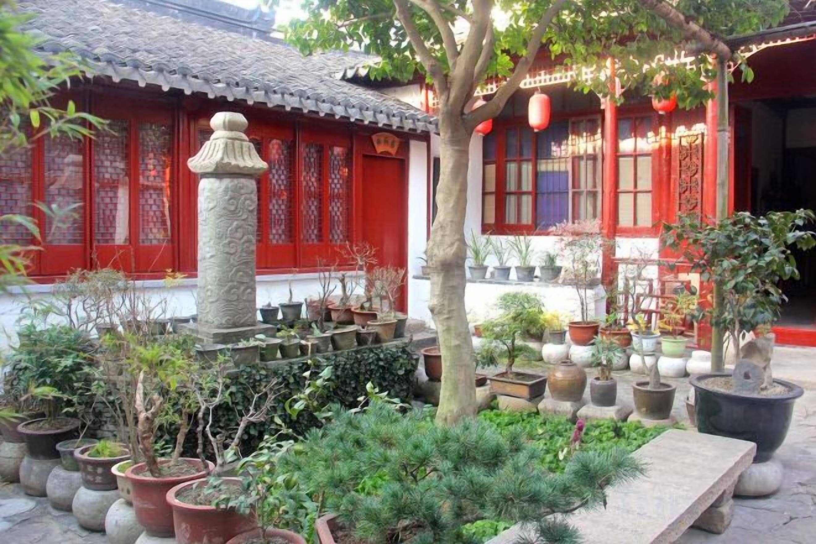 A traditional building with red walls and a tiled roof, surrounded by potted plants and a stone bench.